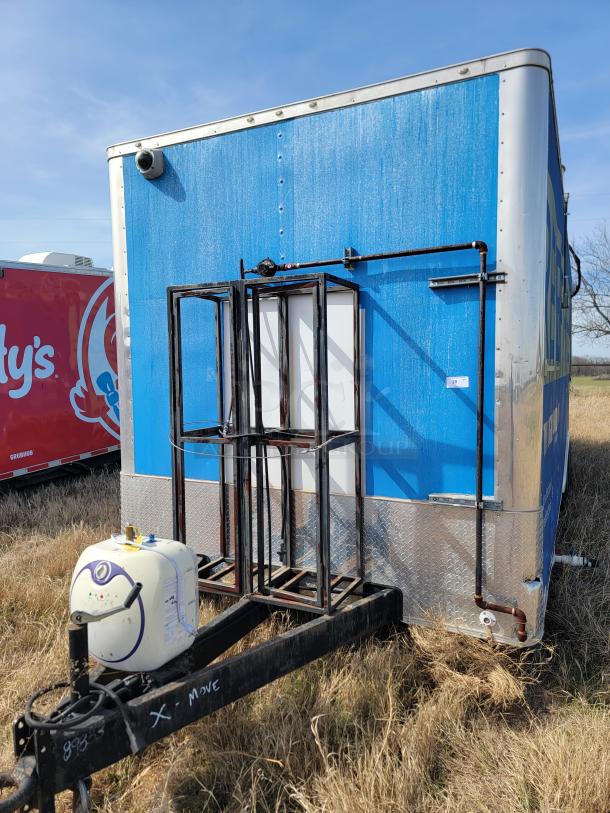 Blue and silver enclosed trailer with pipe fittings and a front-mounted tank. Some rust visible on the metal frame.