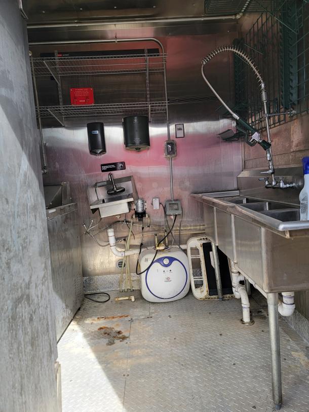 Industrial kitchen setup with stainless steel sink, hose faucet, and shelves. Visible wear and plumbing.