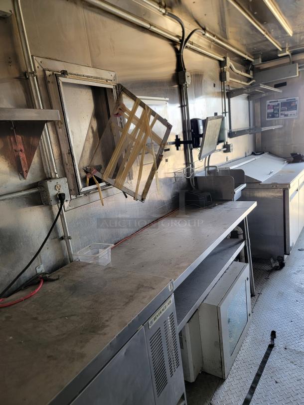 Commercial food truck interior with stainless steel counters, shelving, and ventilation. Includes Beverage-Air refrigeration unit. Worn condition.