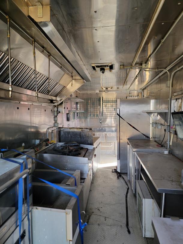 Commercial kitchen trailer interior, stainless steel equipment, ventilation hoods, cooking units, fair condition.