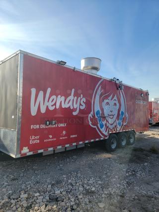Red Wendy's food trailer with ventilation, delivery logos for Uber Eats, DoorDash, Postmates, Grubhub, on rocky ground.