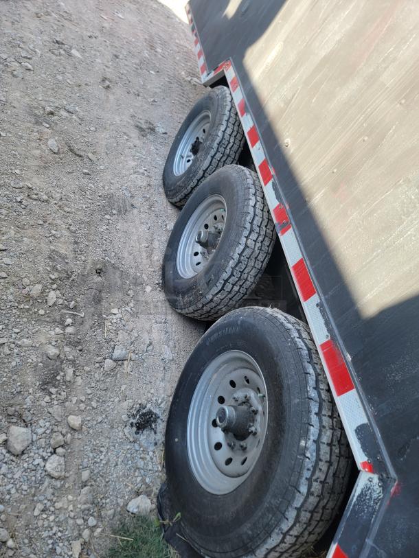 Trailer with three wheels on a gravel path, featuring steel rims and tire brand marking. Condition shows wear.