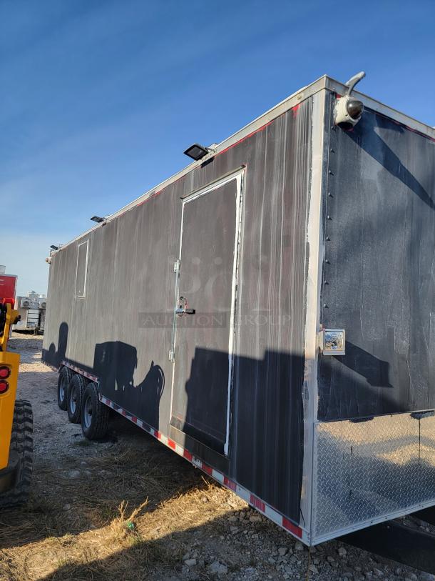 Enclosed triple-axle trailer with weathered exterior, security camera, and floodlights. Diamond plate detailing on front.