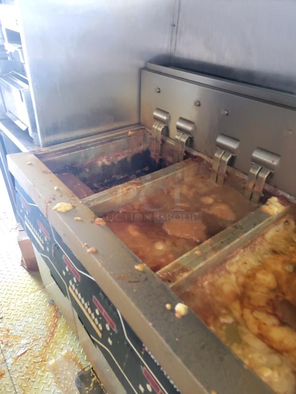 Commercial deep fryer with four baskets, stainless steel, used condition, visible residue and grease, industrial kitchen setting.