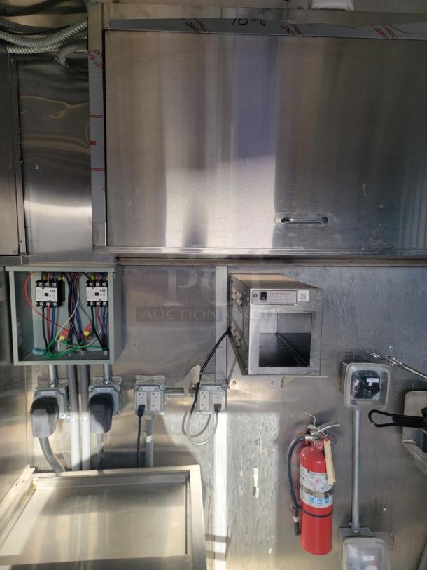 Interior view of a stainless steel industrial kitchen setup with wiring, electrical outlets, and a mounted fire extinguisher.