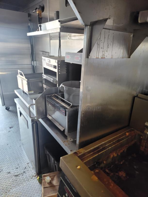 Commercial kitchen equipment setup, including fryers, stainless steel shelves, and ovens. Functional, used condition.