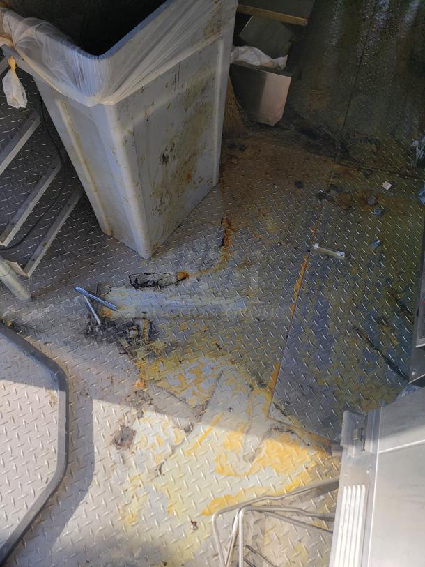 Trash bin and damaged metal floor with rust and debris, showing neglect and poor condition, no visible tags or labels.