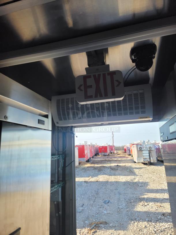 Interior view of a commercial trailer with an illuminated "EXIT" sign, air curtain, and camera, leading to a yard of red trailers.
