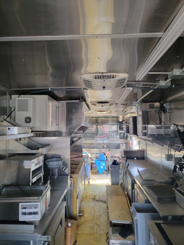 Mobile kitchen interior, featuring commercial-grade stainless steel appliances, ventilation, and storage. Clean, well-maintained condition.