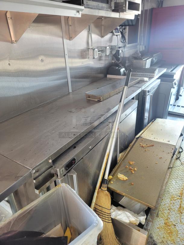 Commercial stainless steel kitchen workstation, shows signs of use; includes stainless prep table, broom, and cutting board.
