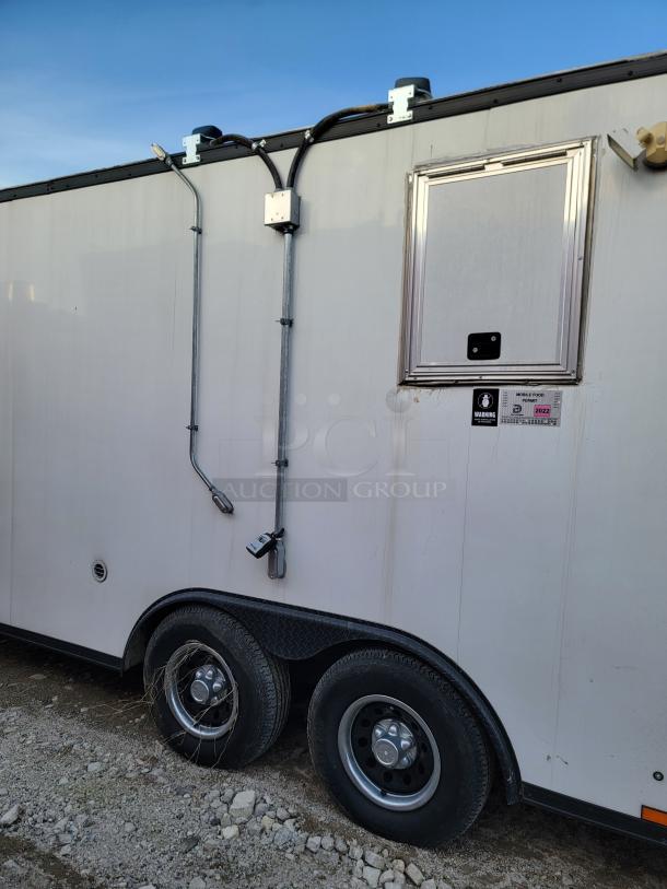 White utility trailer with dual axles, external electrical wiring, and a small window. Visible 2022 mobile food unit tag.