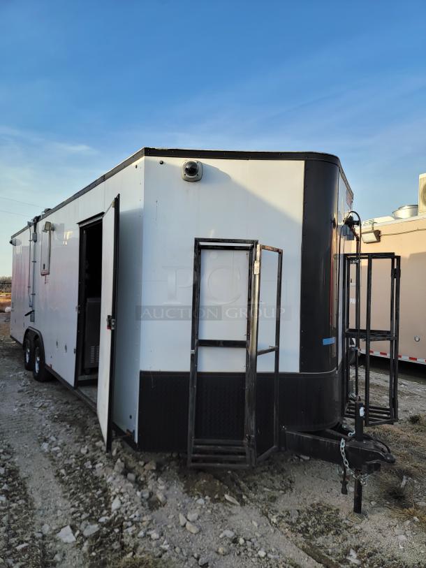 White and black enclosed trailer on rocky terrain, open side door, visible vent and hitch, good condition.