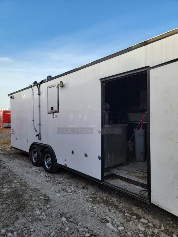 White dual-axle trailer with open side door, revealing interior equipment and storage. Appears in good condition.