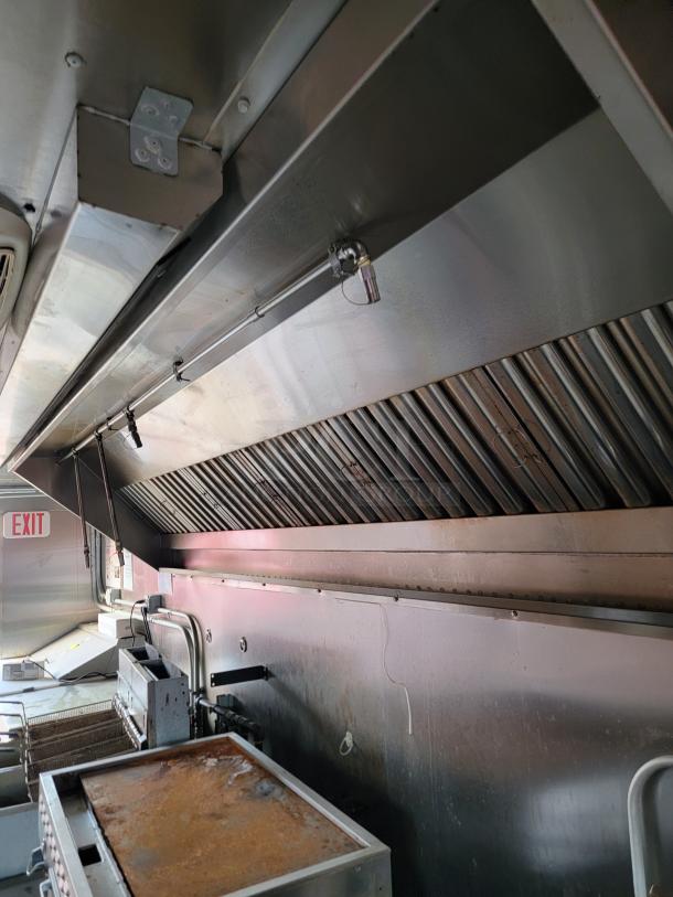 Commercial kitchen exhaust hood with stainless steel construction, angled baffle filters, and internal lighting, in used condition.