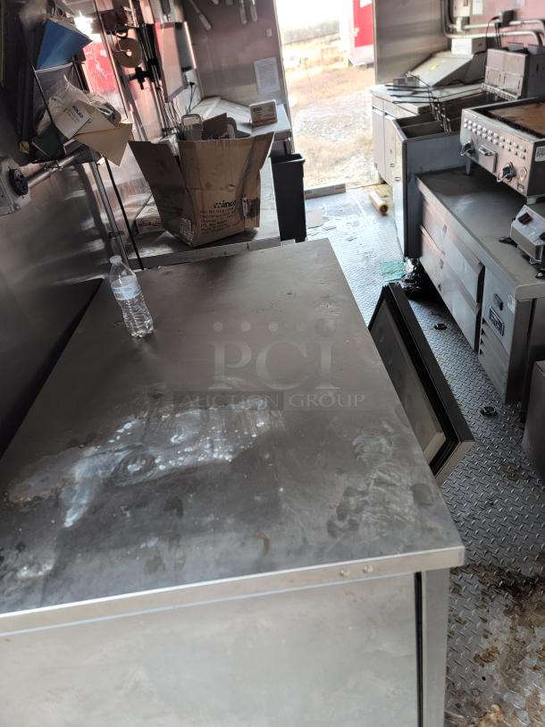 Commercial kitchen interior with stainless steel countertops, storage units, and cooking equipment. Used condition, visible wear.