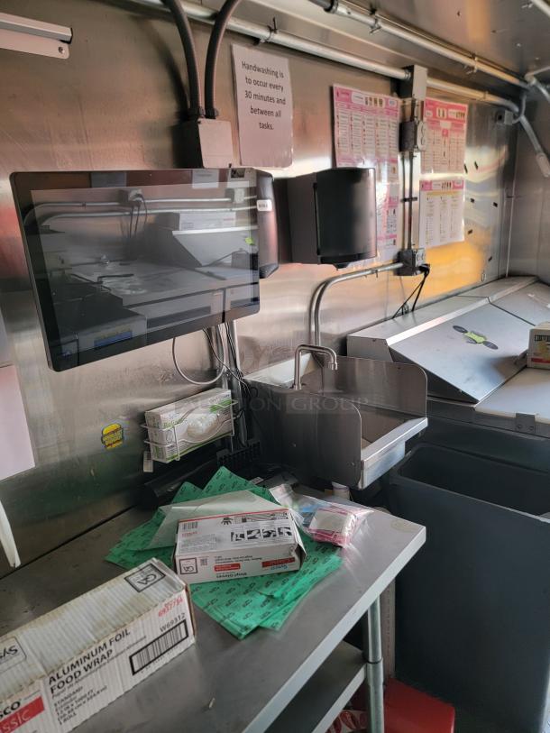 Stainless steel workstation with a monitor, handwashing sign, and various packaging supplies. Clean, organized setup.