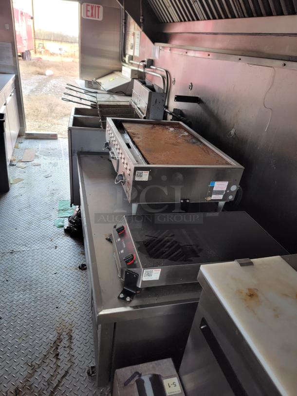Commercial kitchen equipment including griddles and fryers. Used condition with visible grease and wear. Safety exit sign visible.