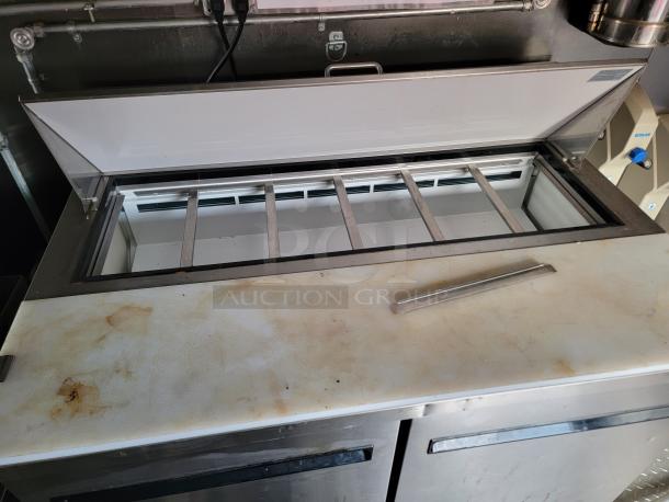 Commercial refrigerated prep table, stainless steel, used condition with visible surface stains and open top storage area.