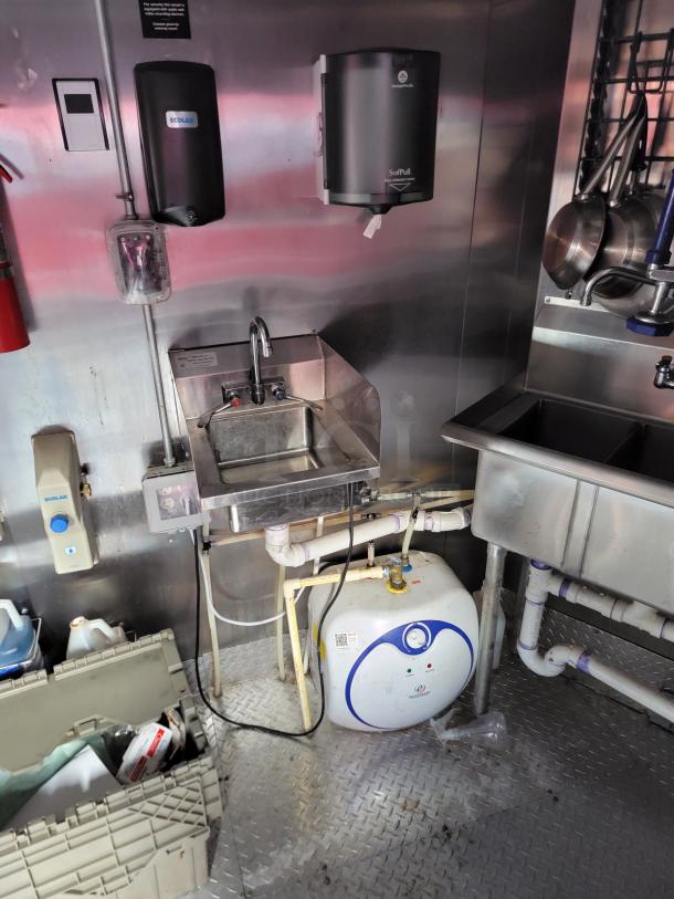 Commercial kitchen setup with a stainless steel hand sink, wall-mounted soap and paper towel dispensers, and an under-sink water heater.