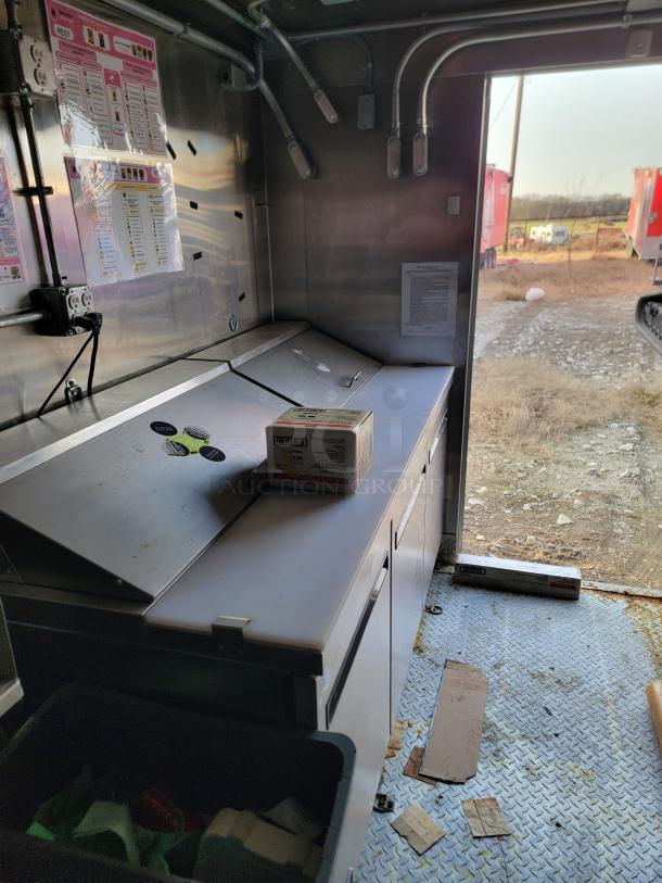 Interior view of a stainless steel commercial kitchen unit with countertop and storage. Menu labels and electrical outlets visible.