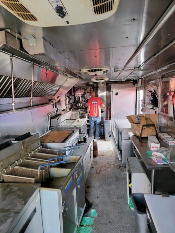 Interior of a commercial kitchen in a mobile food truck, featuring deep fryers, grill, and stainless steel counters.