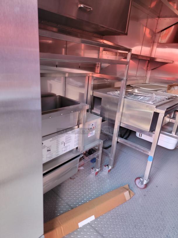 Commercial kitchen equipment on a metal floor, featuring stainless steel shelves and storage units, in unused condition.