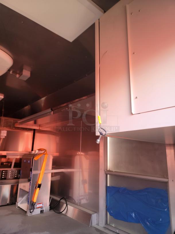 Interior of a commercial kitchen trailer with stainless steel surfaces, equipment secured with orange straps, and a covered storage area.