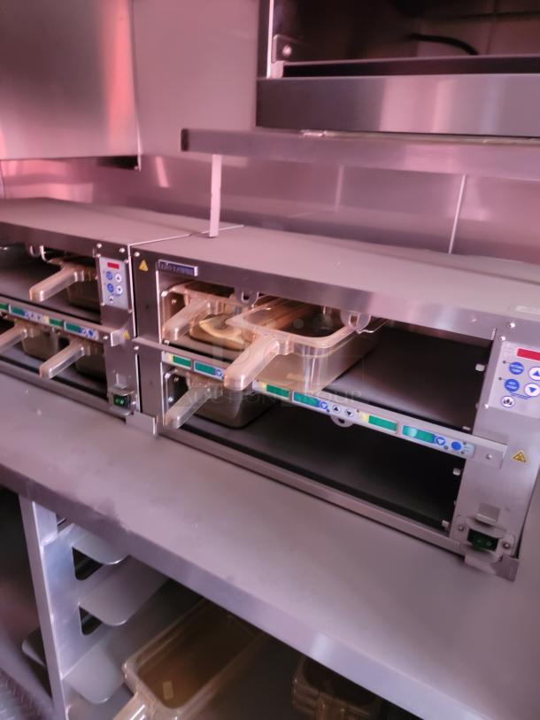 Commercial food warming units with digital controls, stainless steel finish, and clear food trays in a restaurant kitchen setting.