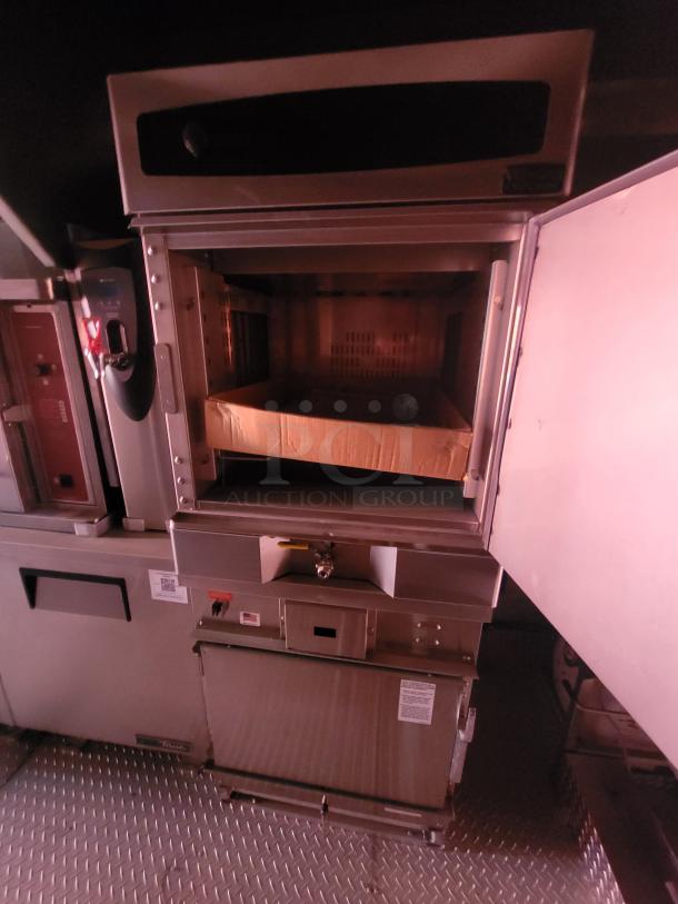 Commercial-grade oven with open door, metal finish, control panel, and visible internal compartment. Markings indicate operating instructions.
