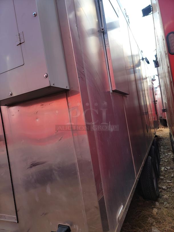 Large metal trailer, reflective surface, dual axle tires, visible panel with hinges, minor surface scratches, outdoor setting.