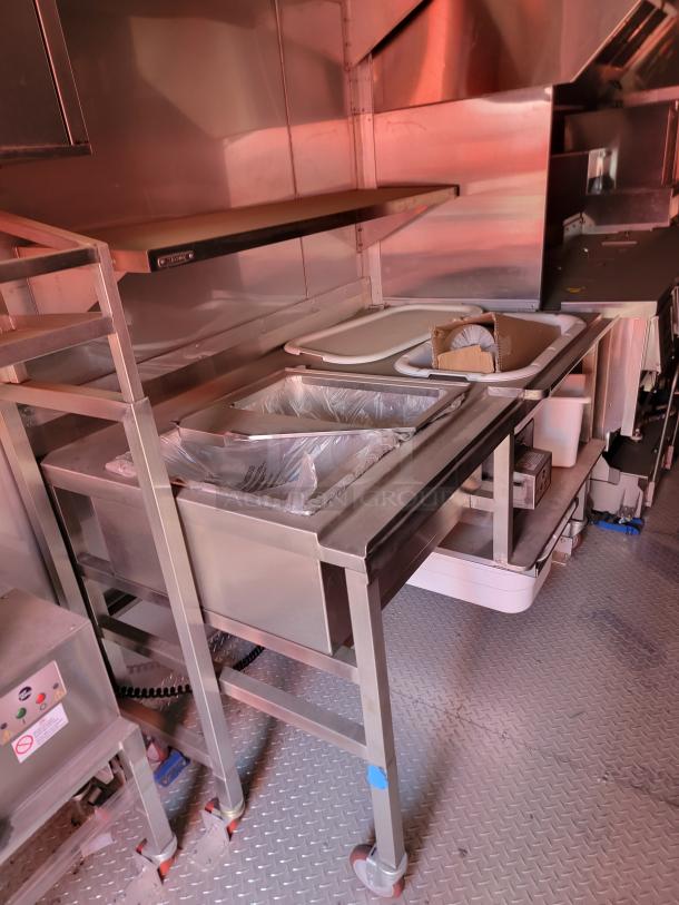 Commercial stainless steel kitchen prep station with attached sink, shelving, and visible control panel. Suitable for food service use.