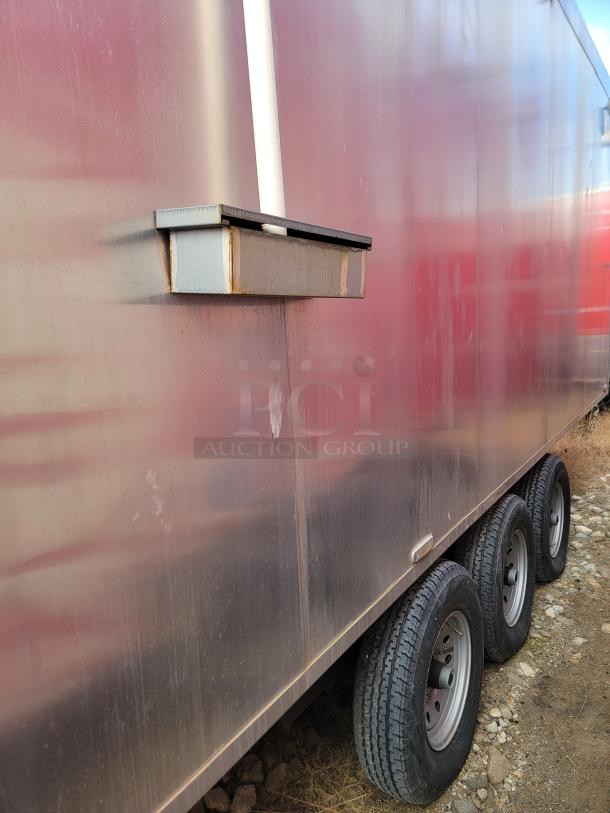Mobile trailer with triple axle, metal siding, visible rust, and mounted structure. Appears to be in fair condition.