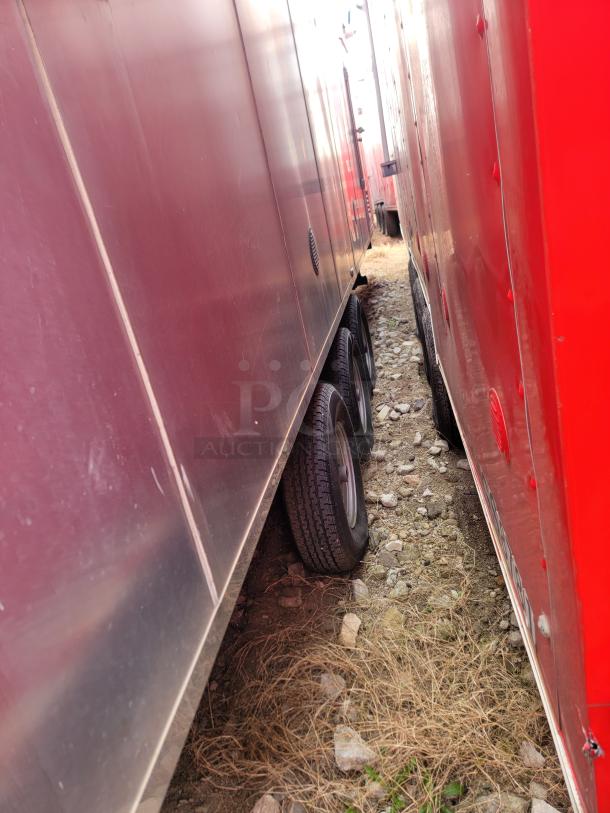Red and silver trailer side view showing dual tires on rocky ground. Condition appears used with some surface wear.