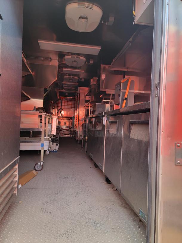 Interior view of a stainless steel commercial kitchen trailer with ventilation units, industrial equipment, and metal surfaces.
