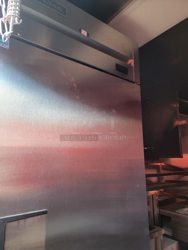 Stainless steel commercial refrigerator, True brand, visible logo and control panel, in a kitchen setting.