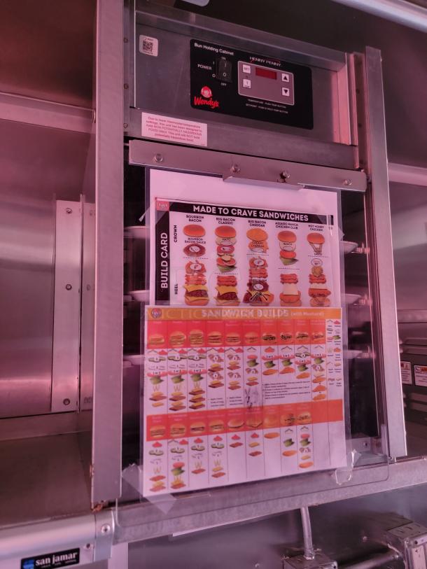 Commercial bun holding cabinet with Wendy's logo and sandwich build guide on door. Henny Penny model, stainless steel finish.