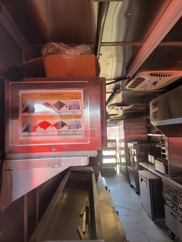Interior view of a commercial kitchen trailer featuring stainless steel appliances, preparation stations, and storage units. A Chili Batch Preparation chart from Wendy's is visible on a screen.
