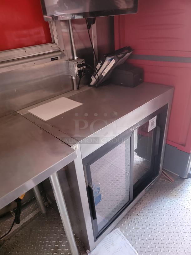 Stainless steel commercial refrigerator with glass door, brand "True," in excellent condition, visible label on door.