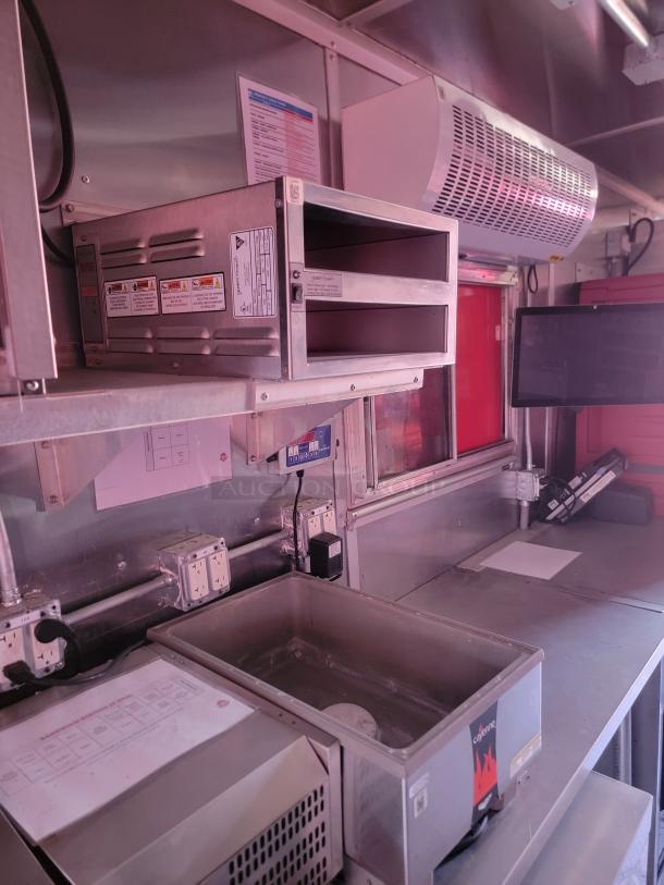 Commercial kitchen setup featuring a stainless steel double rack oven, ventilation unit, control panel, and various safety labels.
