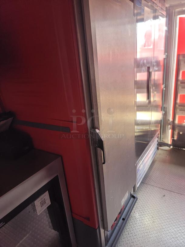 Red and silver commercial refrigerator with a black handle, situated on a diamond plate floor, in good condition. Visible QR code on lower appliance.