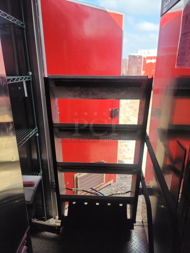 Metal storage shelves inside red container with open door; sturdy frame, adjustable shelving, good condition, suitable for heavy items.
