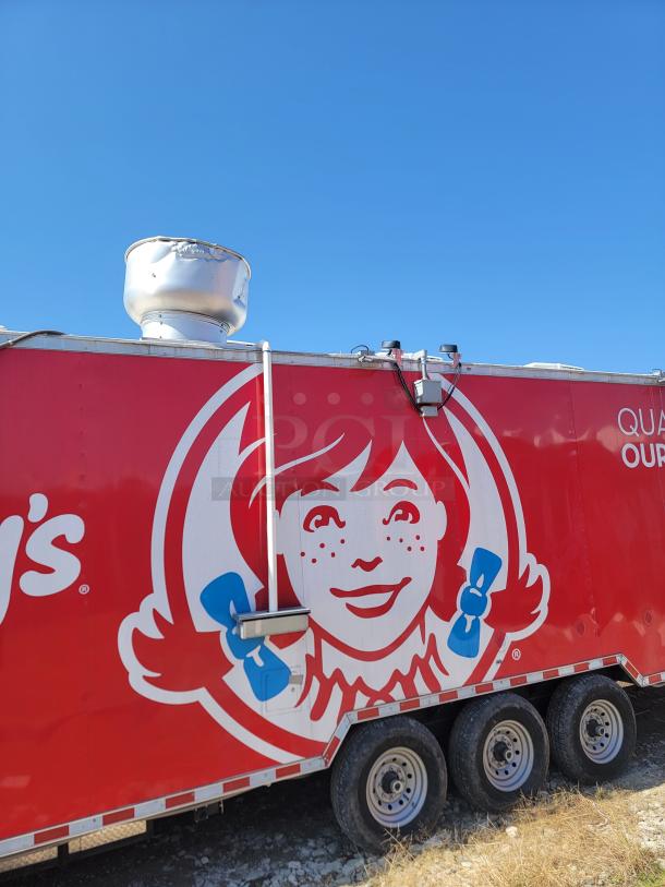 Red food truck with Wendy's logo, three axles, and rooftop vent, parked on gravel.