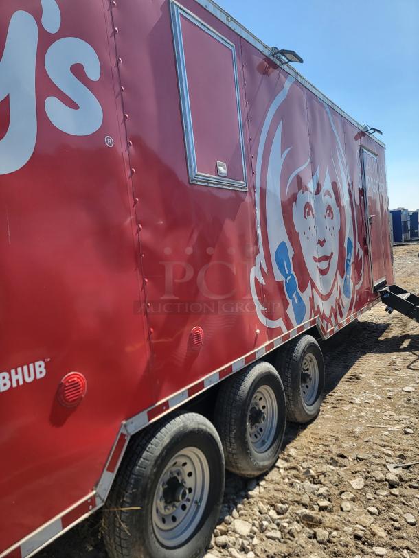 Red mobile food trailer with branded logo, triple axle wheels. Suitable for catering events. Condition appears used.