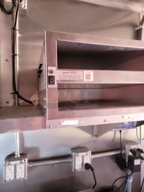 Stainless steel food warmer with power switch, mounted above electrical outlets, in excellent condition. Labels detail heat levels.