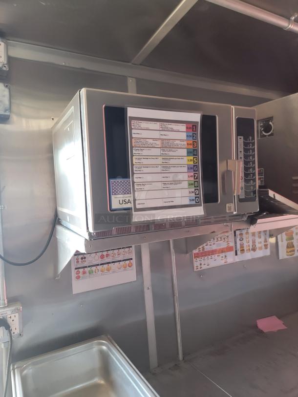 Commercial microwave oven mounted on a metal shelf, control panel with numeric buttons, and a cooking guide on the door.