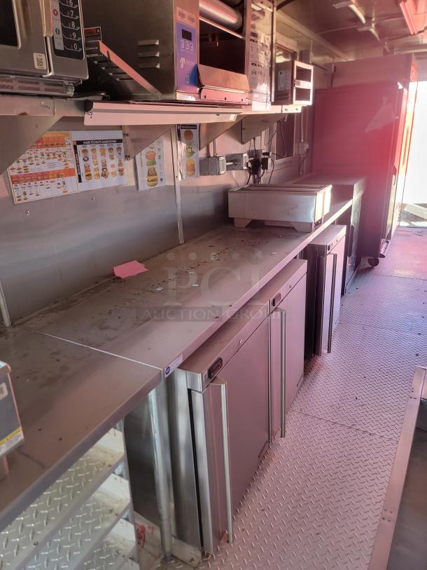 Stainless steel food truck interior with commercial kitchen equipment, including shelves and cabinets. Used condition with visible wear.