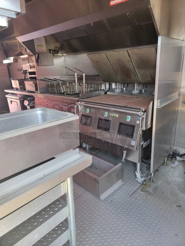 Commercial kitchen equipment in a stainless steel setup, featuring deep fryers and a flat grill. Used condition, visible signage.