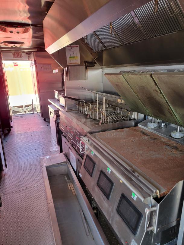 Commercial kitchen interior with stainless steel appliances, fryer baskets, and ventilation hood. Visible wear, but functional.