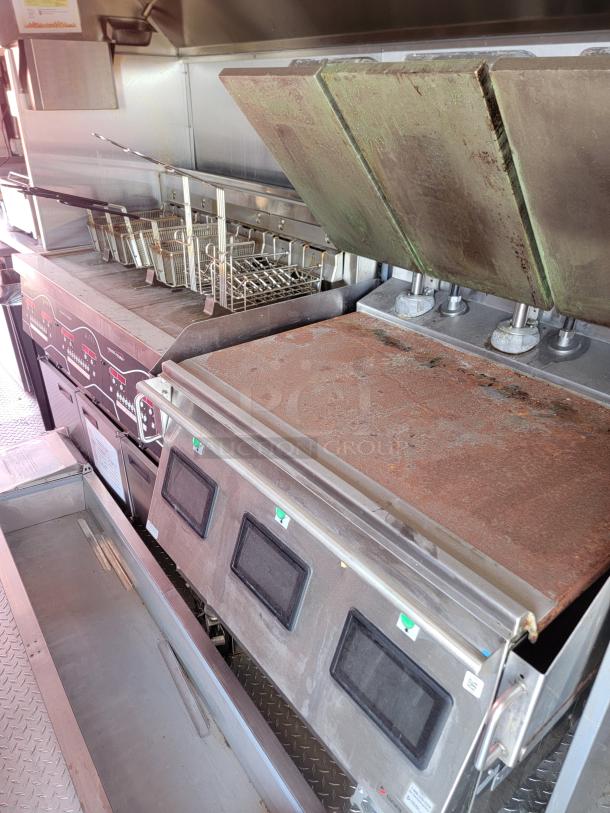 Commercial deep fryer with multiple frying baskets and rusted griddle. Stainless steel surface, used condition.