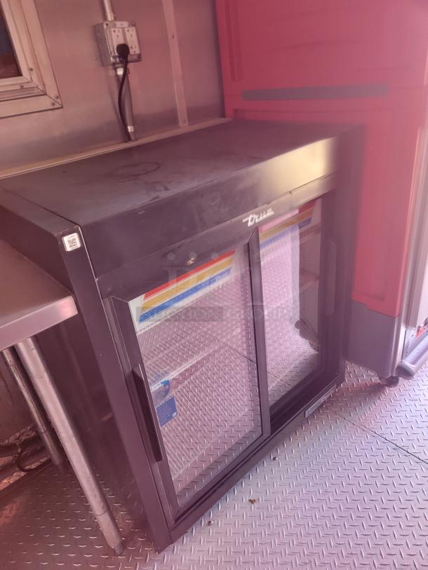 True double-door beverage cooler, black finish, glass front, used condition, visible wear. Perfect for commercial use.